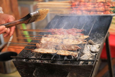 Cropped hand of person preparing meat on barbecue grill 