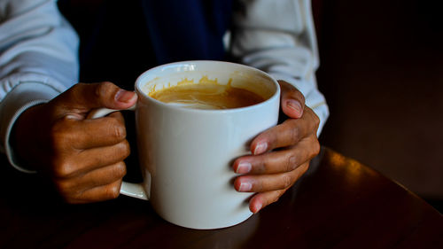 Midsection of person holding coffee cup on table