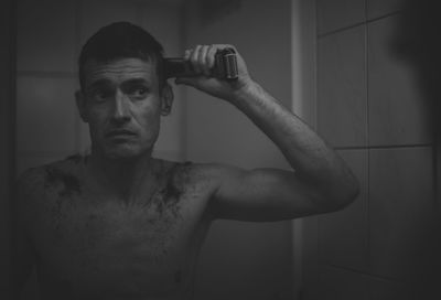 Shirtless man doing haircut in bathroom