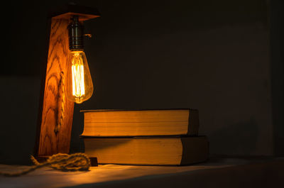 Illuminated light bulb on table against wall at night