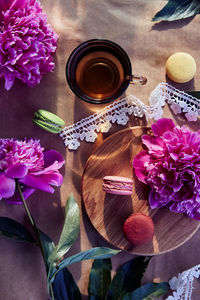 Macarons dessert, black tea among blooming peony flowers under trendy hard shadows in the terrace.