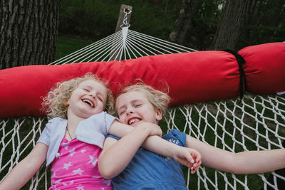 High angle view of happy sisters lying on hammock at yard