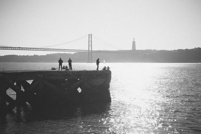 Silhouette people standing on suspension bridge over river