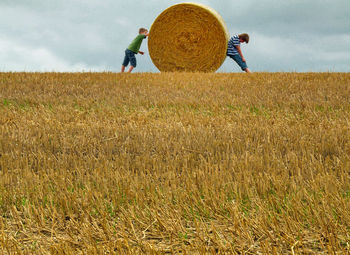 Boys standing with hay bale on agricultural field