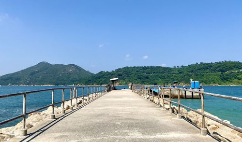 Rear view of pier over sea against blue sky