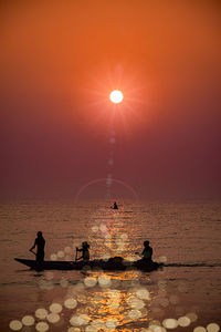 Silhouette people by sea against sky during sunset