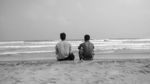 Rear view of men sitting on beach
