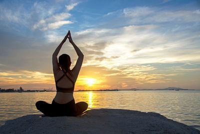 Woman relaxing in sea against sky during sunset