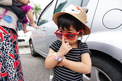 Cute girl wearing sunglasses and hat standing against car