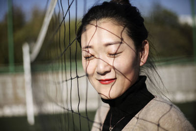 Close-up of young woman by sports net