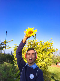 Portrait of smiling young woman with yellow flower against clear blue sky