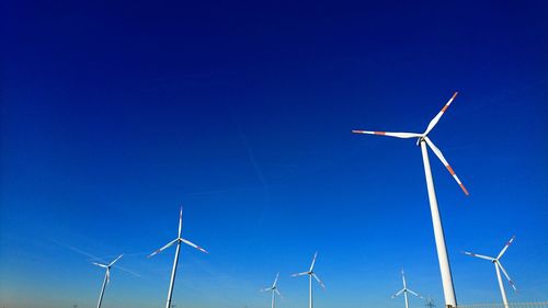 Low angle view of windmills against clear blue sky