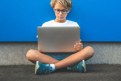 Boy using laptop on footpath