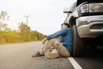 Man sitting on road by street against sky