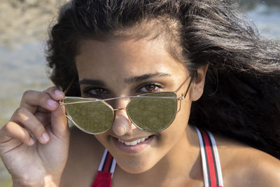 Close-up portrait of smiling young woman holding sunglasses