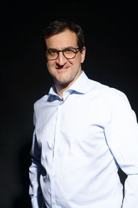 Portrait of young man standing against black background