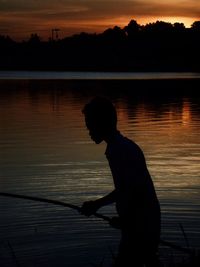 Silhouette man standing by lake against sky during sunset