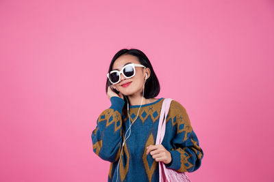 Portrait of young woman wearing sunglasses standing against pink background