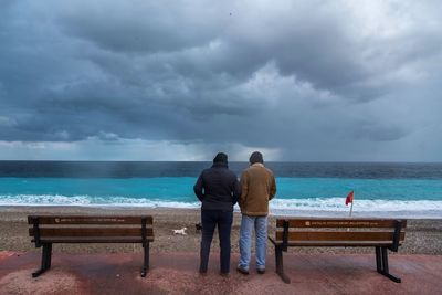 Rear view of men sitting on beach against sky