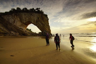 People on rock formation at beach against sky