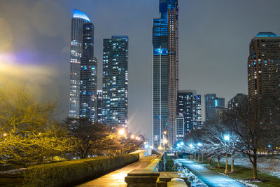 Illuminated street amidst buildings against sky at night