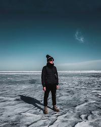 Full length of man standing in sea against sky during winter