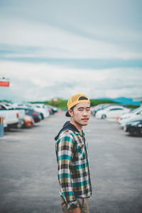 Side view portrait of young man standing on street against sky