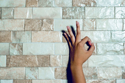 Cropped hand of person gesturing ok sign against wall