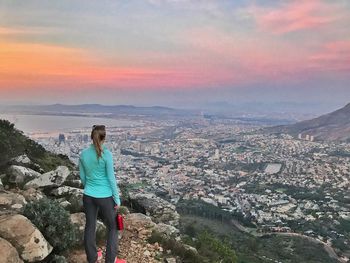 Rear view of woman standing on rock against sky during sunset