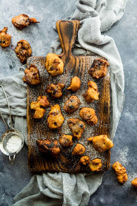 A wooden board topped with fruit filled fritters sprinkled with icing sugar.