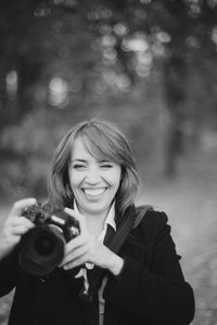 Portrait of smiling woman holding camera outdoors