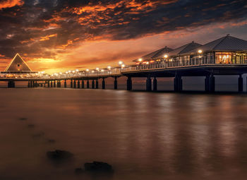 Illuminated bridge over sea against sky at sunset