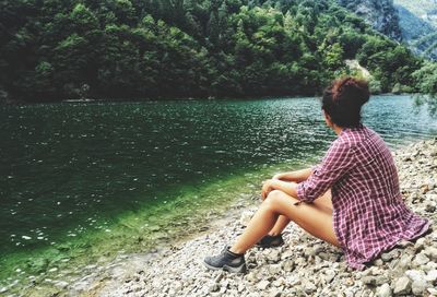 Woman sitting by lake against trees