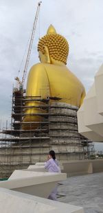 Rear view of man sitting outside building against sky