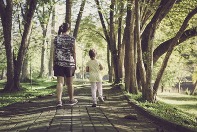 Rear view of mother and daughter walking on footpath at park