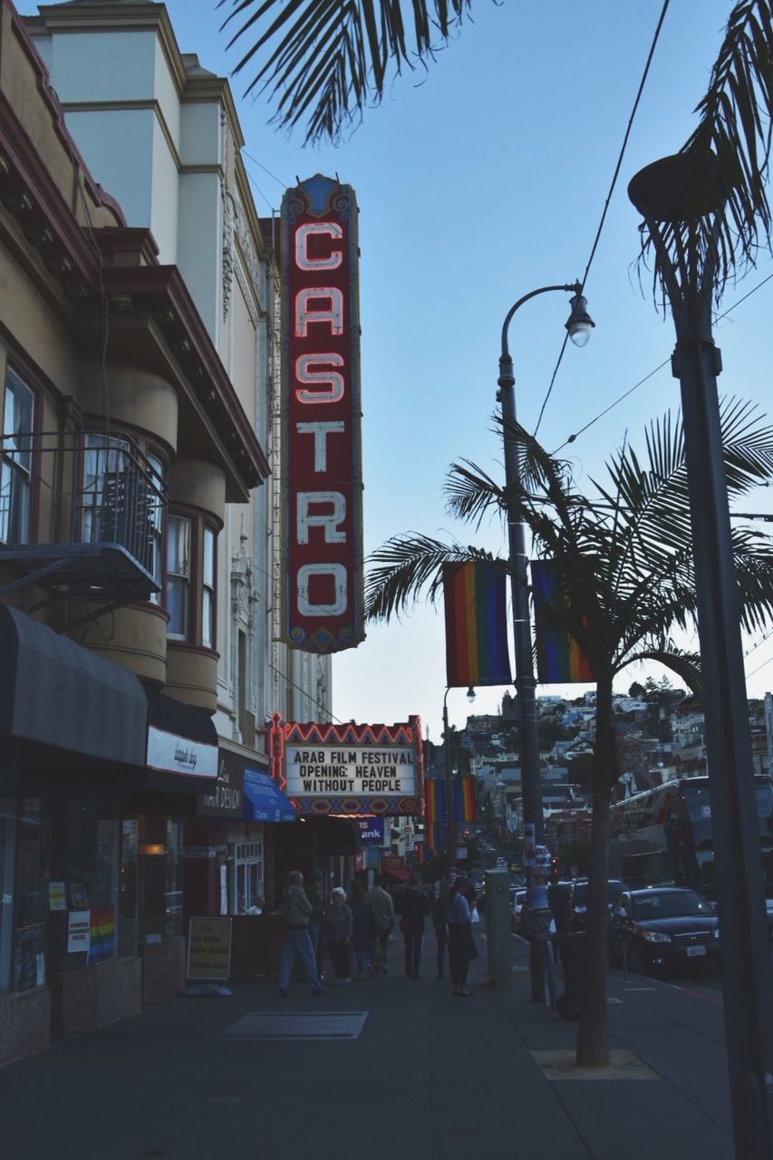 city, street, palm tree, building exterior, communication, architecture, tropical climate, built structure, tree, sign, sky, text, group of people, road, city street, western script, nature, building, day, city life, outdoors