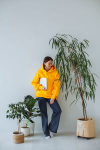 Young woman standing at home near white wall with laptop