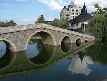 Arch bridge over lake by buildings against sky