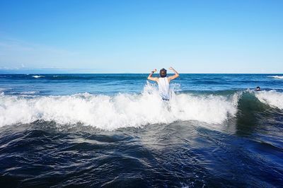 Rear view of man enjoying waves in sea against sky