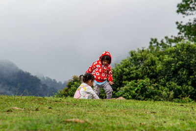 Siblings playing on grass against sky