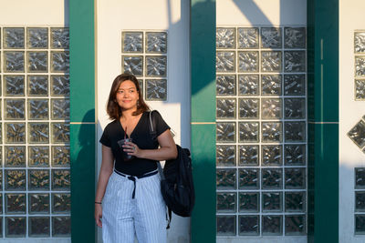 Portrait of young woman standing against window