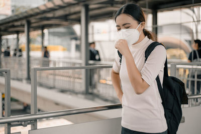 Woman looking away wearing pollution mask while standing on footbridge