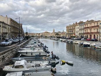 Boats moored in river by buildings in city against sky