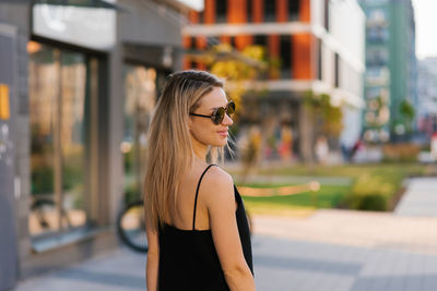 Happy smiling blonde woman in a black dress walks in the city in summer