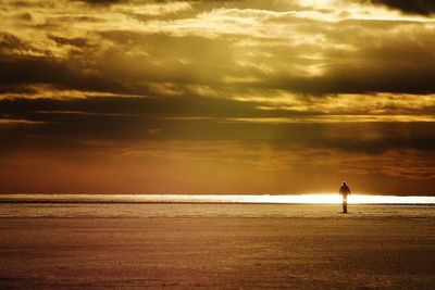 Silhouette person standing at beach against cloudy sky during sunset