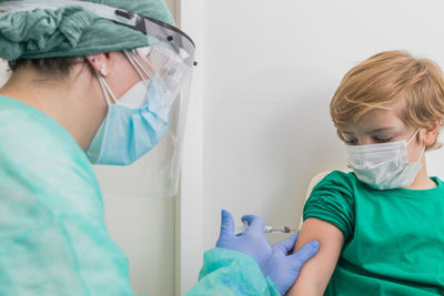 Medic in protective uniform and with sterile syringe giving injection for child from coronavirus