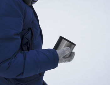 The hand of a man in a winter jacket and mitten holds a tin mug