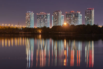 Illuminated buildings by lake against sky in city at night