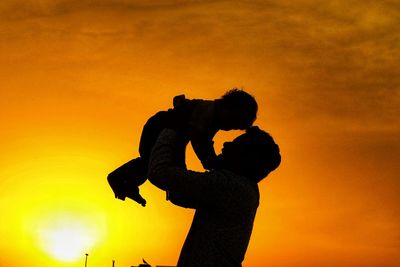 Father carrying baby against sky during sunset
