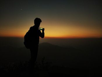 Silhouette man photographing from mobile phone during sunset